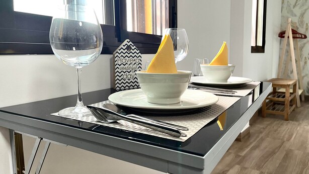 A modern dining area with a glass-top table, white plates, and a clear glass. - New Mosque2-Mezquita Cathedral (Córdoba)