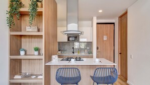 A compact kitchen with a central island, two blue bar stools, wooden shelving with plants, and a microwave. - w* |  Stylish & Cozy Duplex Loft in Zona G (Bogotá)