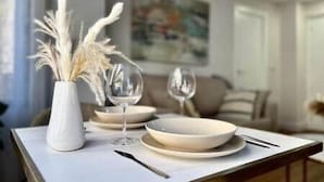 Uma mesa de jantar com pratos brancos, copos de vinho e um vaso com plantas secas.