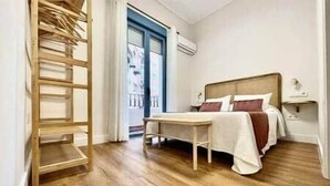 Quarto com cama, escada de madeira e janela com ar condicionado.