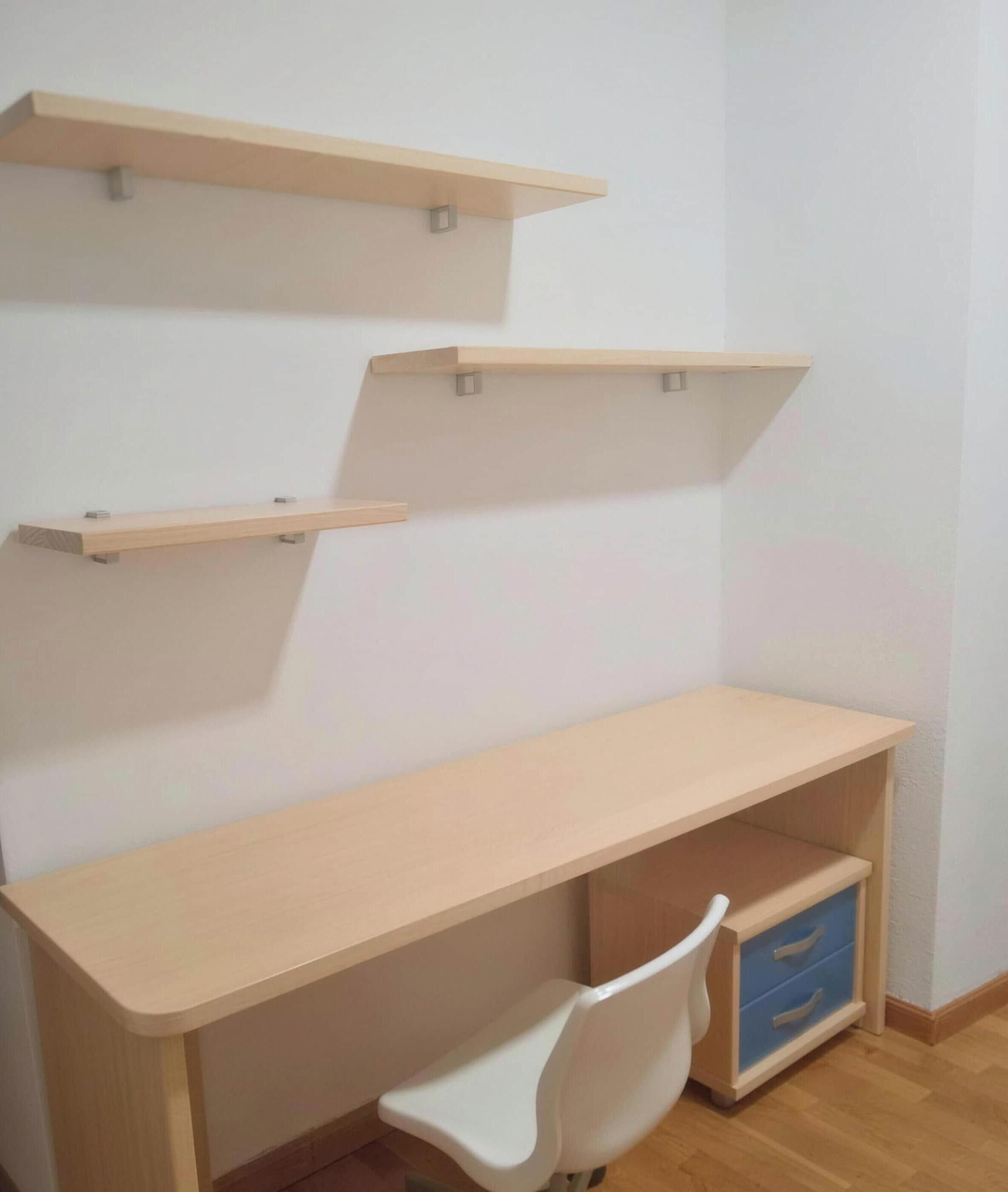 Een kamer met een houten bureau, een witte stoel en twee planken.