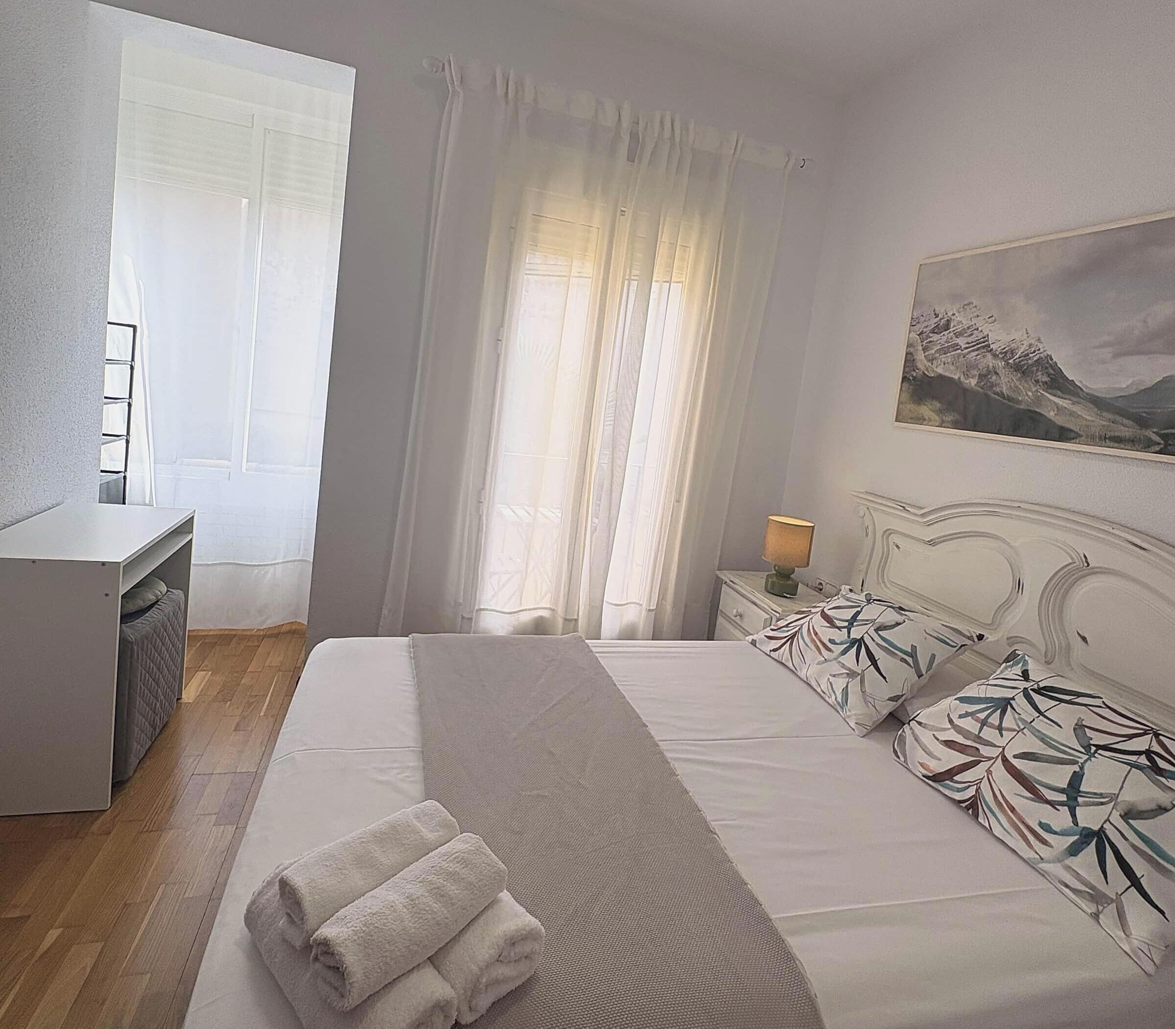 Een hotelkamer met een bed, een bureau, een stoel, een nachtkastje met een lamp en een schilderij aan de muur.