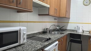 Ett kök med träskåp, en mikrovågsugn, en diskmaskin, en diskho och en klocka på väggen.