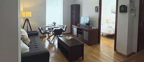 A living room with a sofa, dining table, chairs, a TV, and a cabinet.