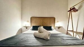 A neatly made bed with a folded towel, a wooden headboard, and bedside lamps. - House in City Garden 3 (Córdoba)