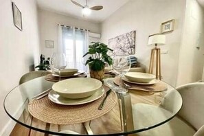 Un coin repas avec une table ronde en verre, dressée pour deux personnes, entourée de chaises.