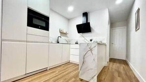 A modern kitchen with white cabinetry, a marble countertop, and a wooden floor. - House in City Garden 3 (Córdoba)