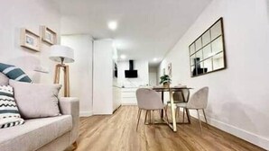 A modern living room with a sofa, a dining table with chairs, and a kitchen area in the background. - House in City Garden 3 (Córdoba)