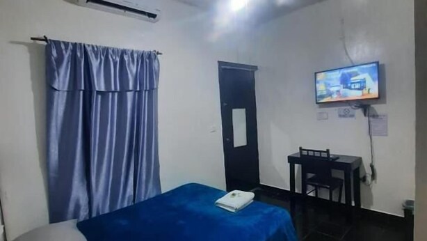 Una habitación con una cama individual, una mesita pequeña, un televisor fijado a la pared y un equipo de aire acondicionado.