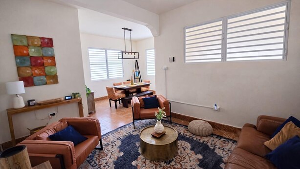 Ein geräumiges Wohnzimmer mit großem Couchtisch, Ledersofas, einem Essbereich mit einer Kronleuchter und einem farbenfrohen Wandbild.