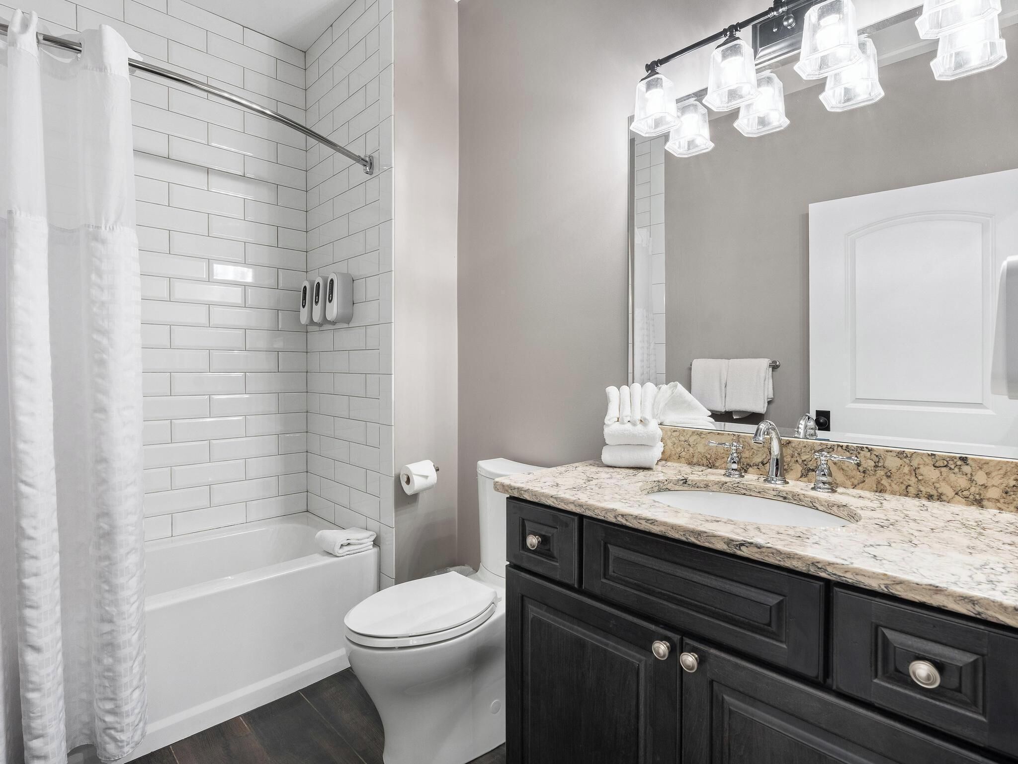 A bathroom with a shower, toilet, sink, and dark cabinets.