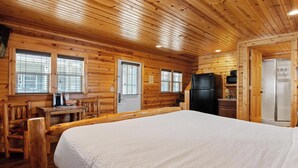 Una habitación tipo cabaña de madera con una cama, un escritorio, un refrigerador y un microondas.