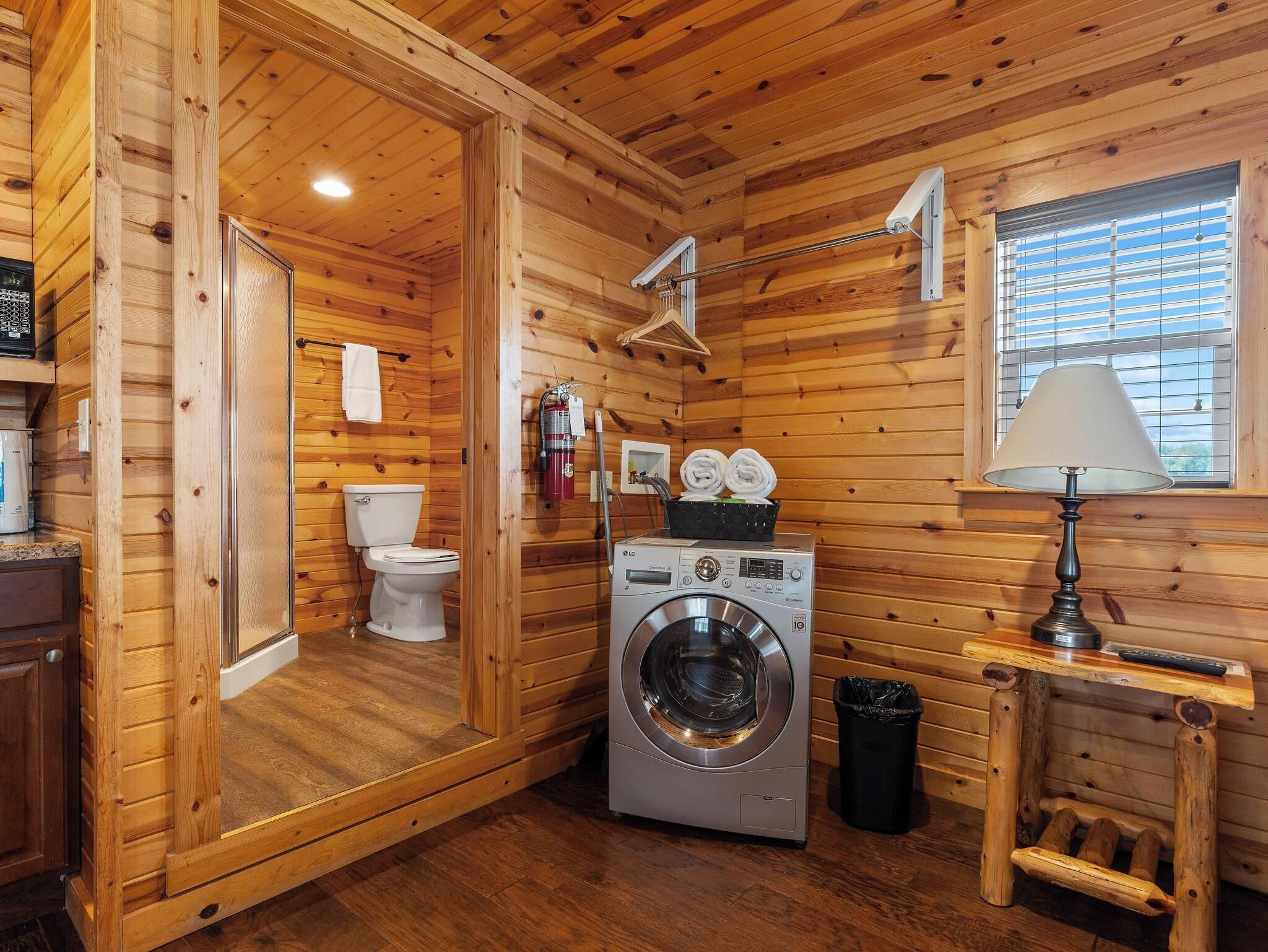 Een compact houten chalet met een zichtbare badkamer, een wasmachine en een raam met zonwering.