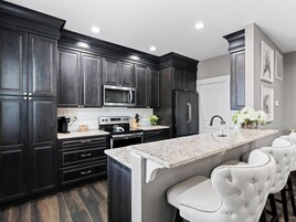 Una cocina moderna con armarios oscuros, electrodomésticos de acero inoxidable, encimera de mármol y una zona de asientos tipo barra.