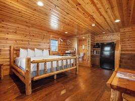 Interior de una cabaña de troncos con una cama de madera, una cocina y un baño.