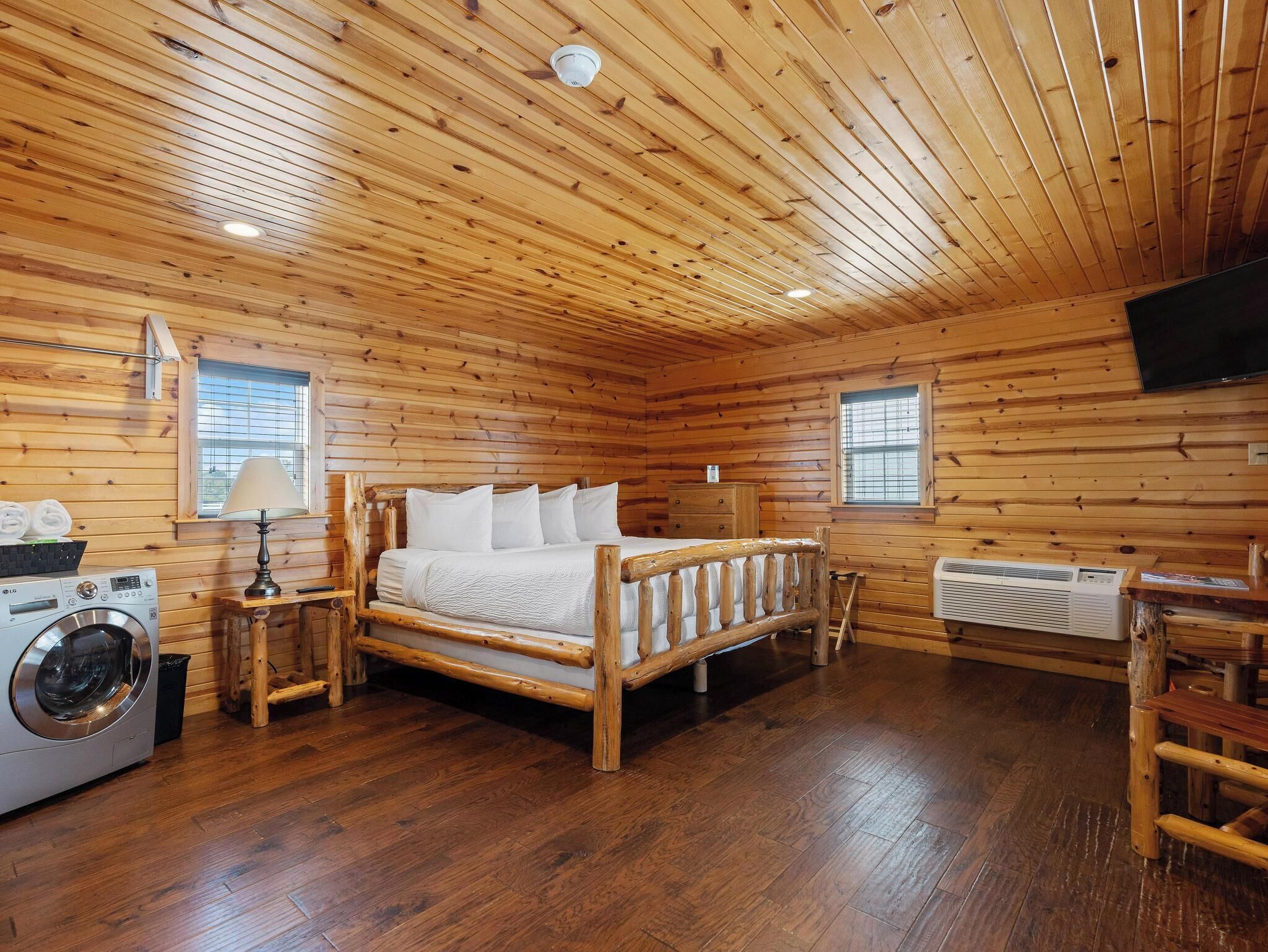 L'intérieur d'une cabane en bois, avec un lit, une machine à laver et un téléviseur.