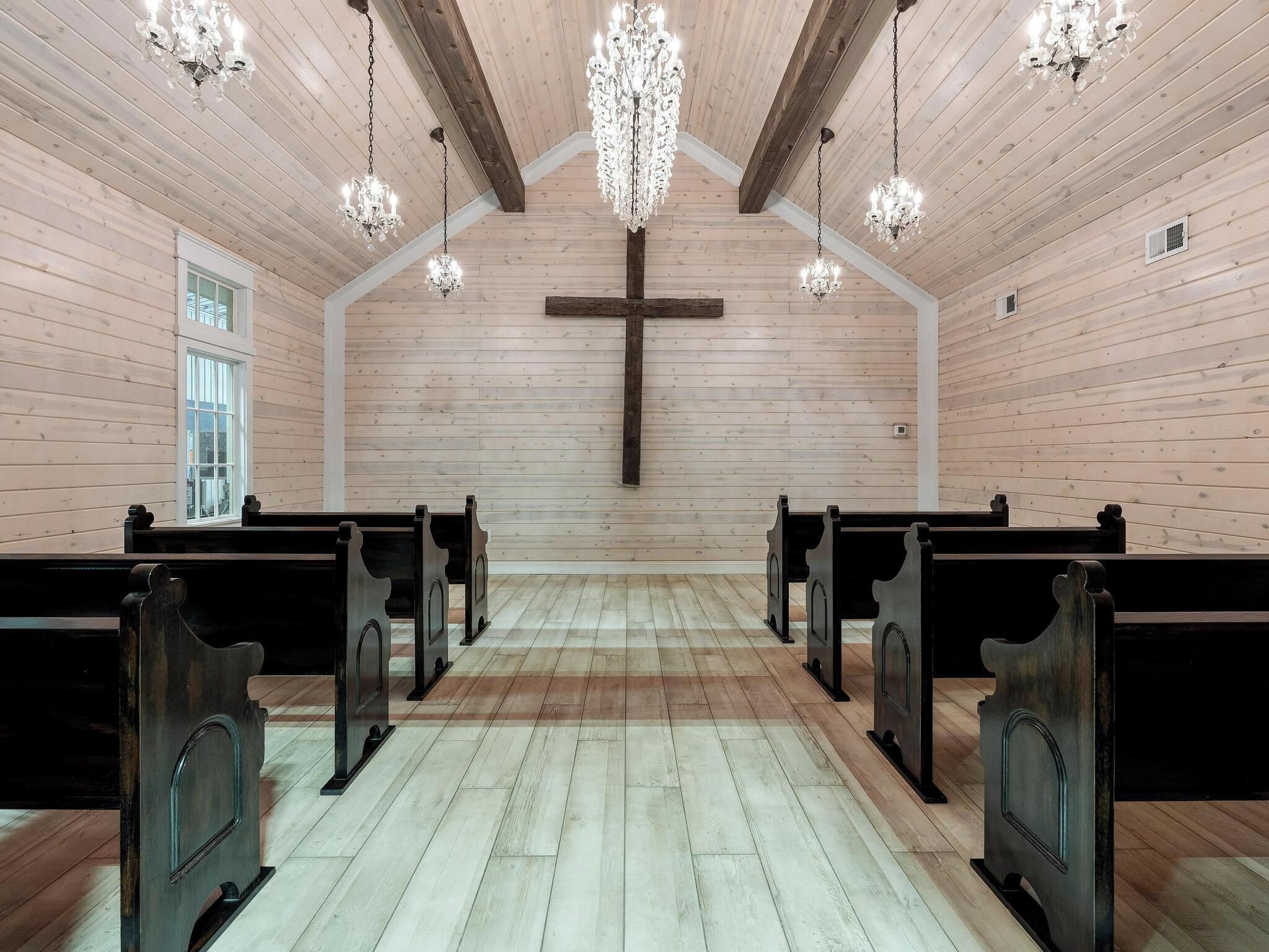 A church interior with wooden pews, a wooden cross, and chandeliers.