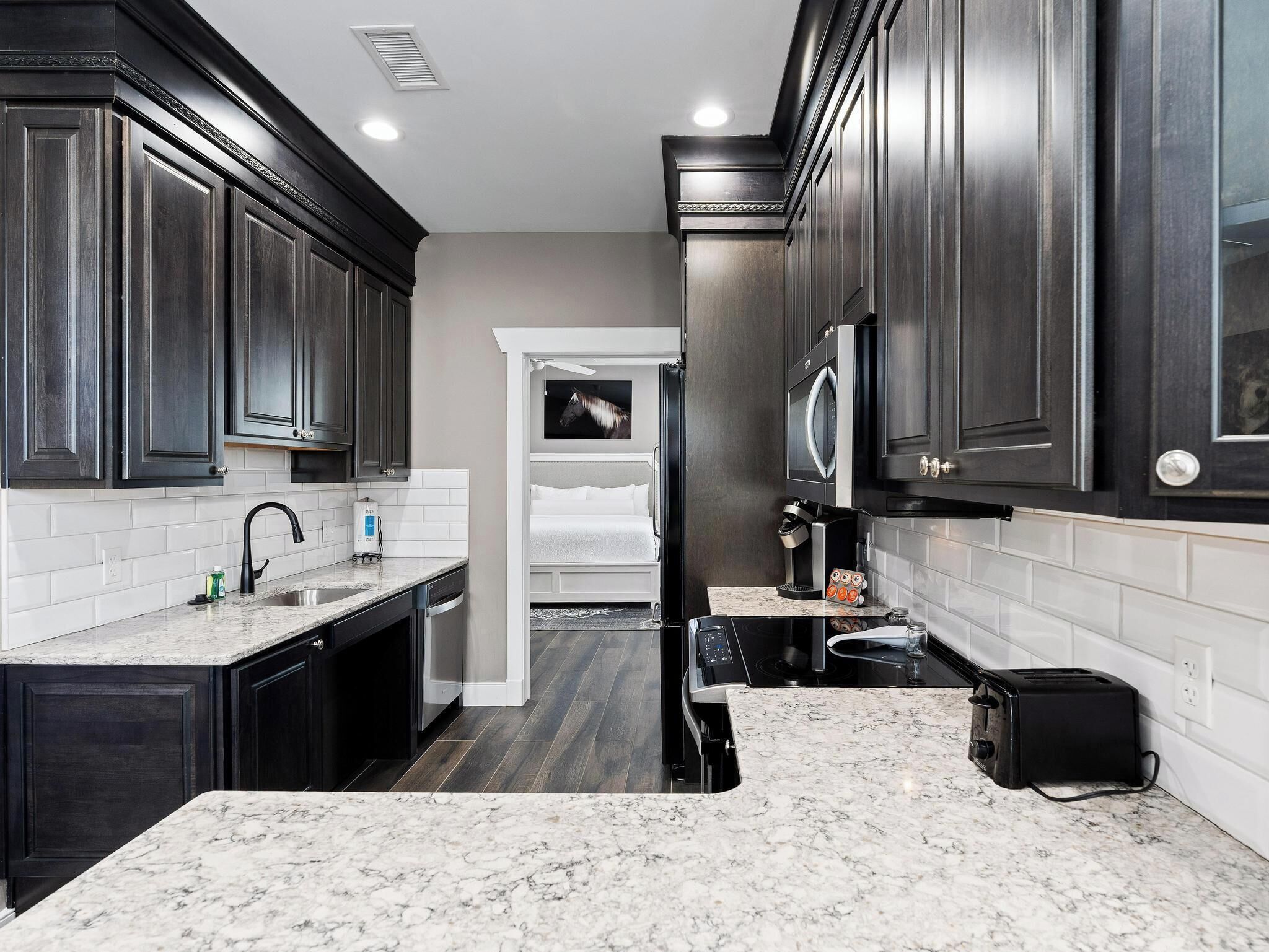 A modern kitchen with dark cabinetry, white subway tiles, and a marble countertop.