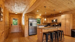 A wooden cabin interior with a kitchen, wooden walls, a refrigerator, a microwave, and bar stools. - Luxury Log Cabin with Hot Tub, Game Room & Theater and Mountain Views (Black Mountain)