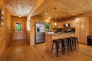 Innenansicht einer Holzhütte mit Küche, Holzwänden, einem Kühlschrank, einer Mikrowelle und Barhocker.