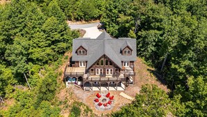 A large, two-story log cabin with a wrap-around porch and a circular seating area. - Luxury Log Cabin with Hot Tub, Game Room & Theater and Mountain Views (Black Mountain)