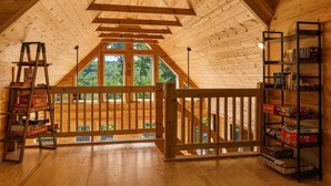 An attic room with wooden beams, a ladder, a bookshelf, and a view of the outdoors. - Luxury Log Cabin with Hot Tub, Game Room & Theater and Mountain Views (Black Mountain)