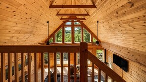 A wooden interior with a sloped ceiling, large windows, and a staircase leading to an upper level. - Luxury Log Cabin with Hot Tub, Game Room & Theater and Mountain Views (Black Mountain)