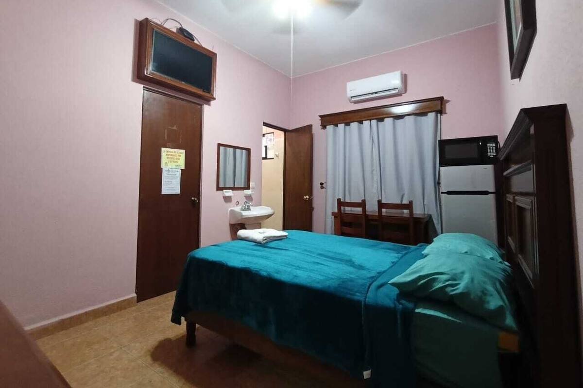 A bedroom with a bed, a desk, a chair, a television, and an air conditioning unit.