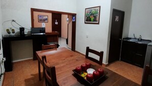 A dining area with a wooden table, chairs, and a tray of apples. There is a kitchen area with cabinets and a sink. - García's Suites y Hotel Villegas (Linares)