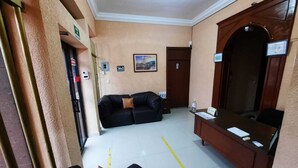 A hotel lobby with a reception desk, a black leather sofa, a wooden bench, and a large mirror. - García's Suites y Hotel Villegas (Linares)