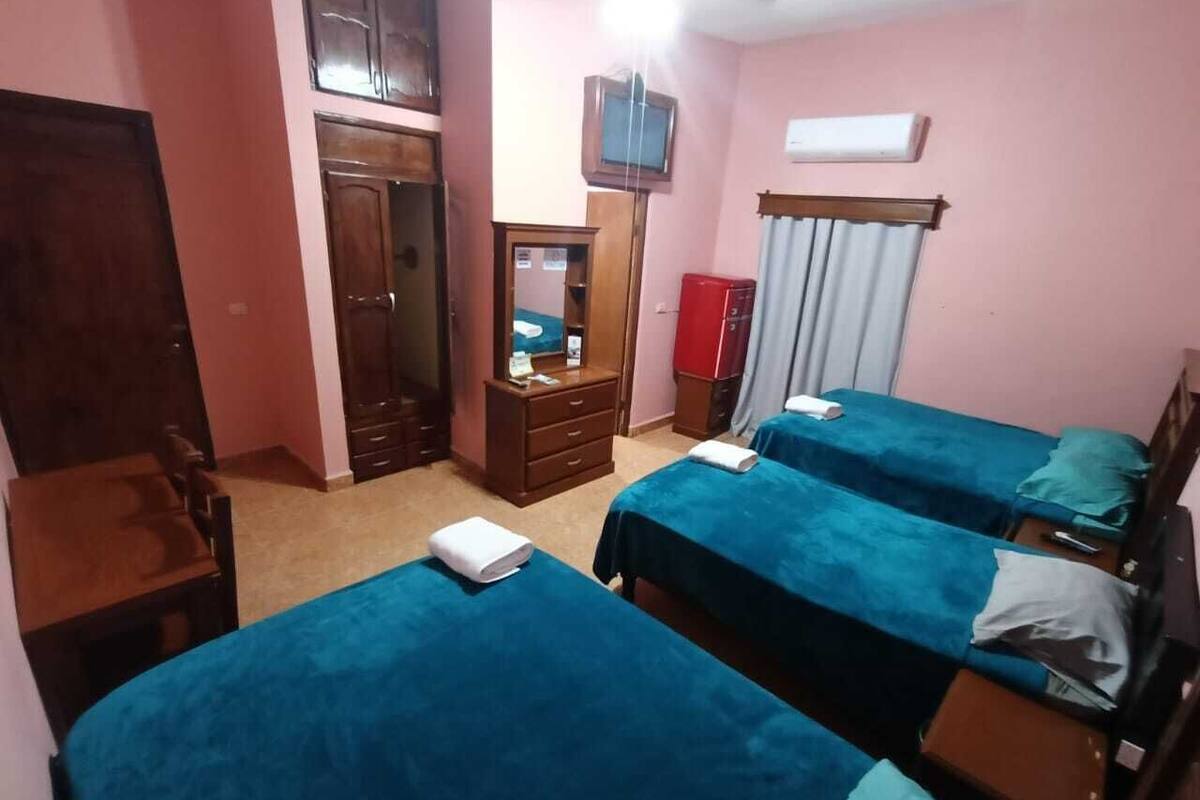 A bedroom with three beds, a wooden wardrobe, a desk, and a television.