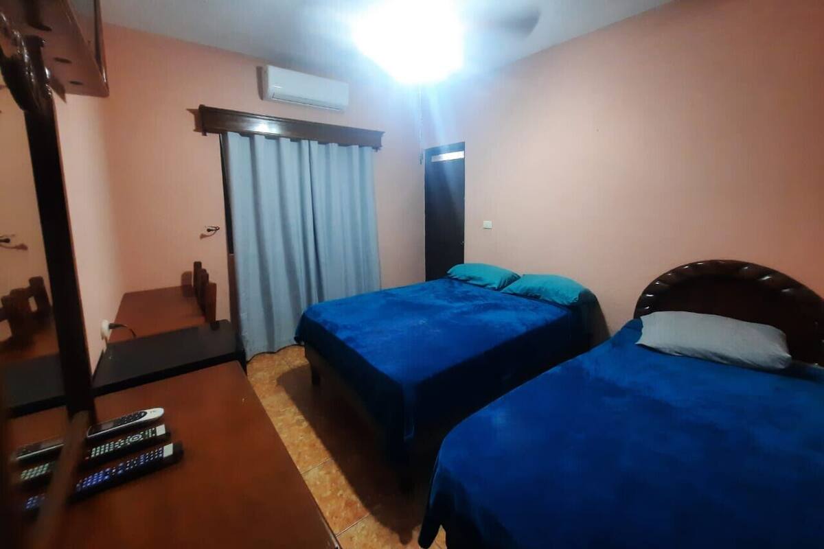 A hotel room with two beds, a desk with a chair, a television, and an air conditioning unit.