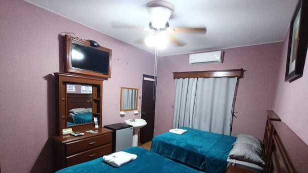 A hotel room with two beds, a desk, a mirror, a ceiling fan, and a TV. - García's Suites y Hotel Villegas (Linares)