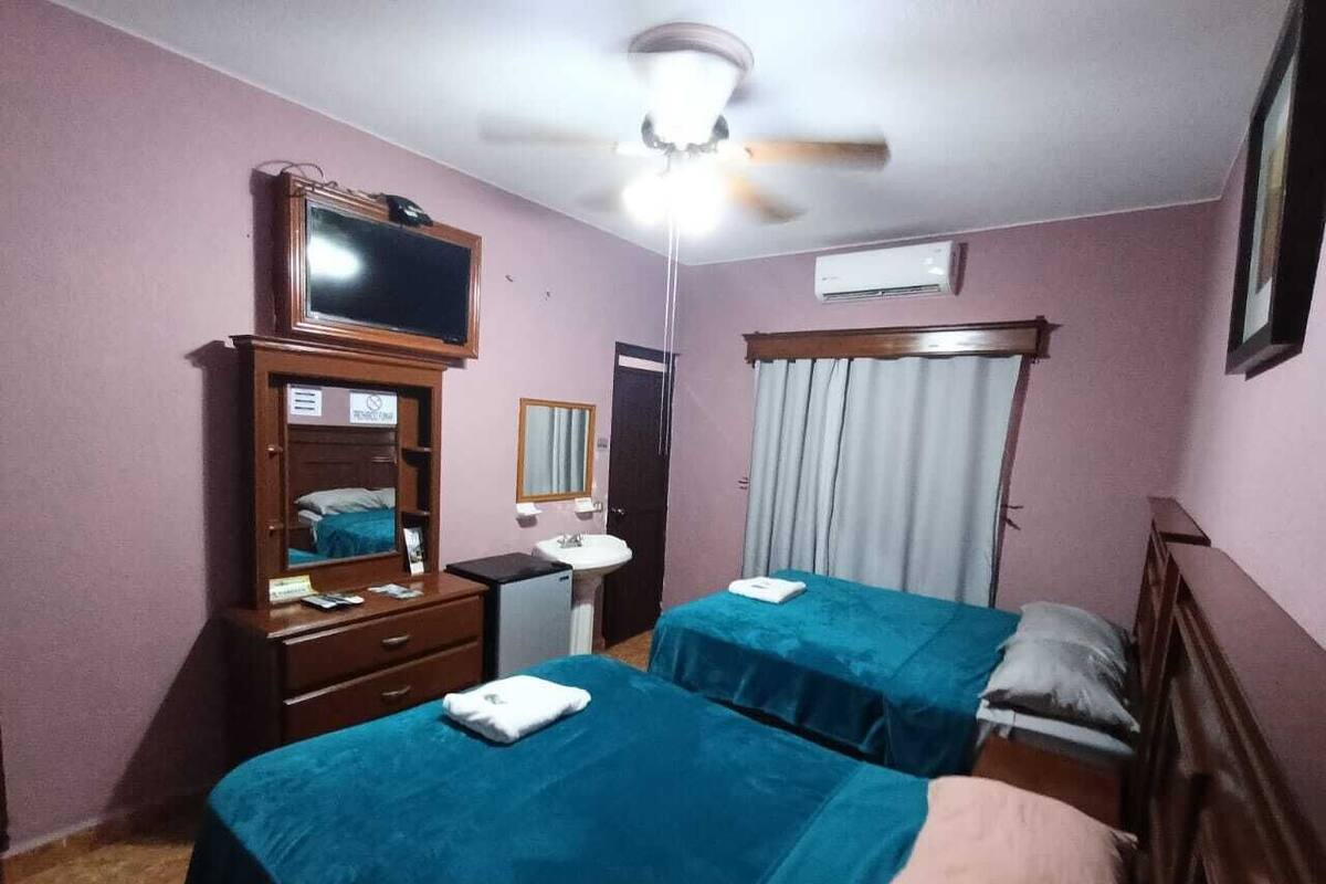 A hotel room with two beds, a desk, a mirror, a ceiling fan, and a TV.