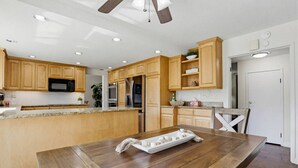 Een moderne keuken met houten kastjes, granieten aanrecht, een centraal eiland, roestvrijstalen apparatuur en een plafondventilator.