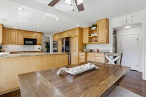 Eine moderne Küche mit Holzausstattung, Granit-Arbeitsplatten, einer zentralen Kochinsel, Edelstahlgeräten und einem Deckenventilator.