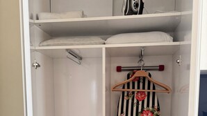 Une armoire blanche dotée de plusieurs étagères, d’une tringle pour suspendre les vêtements et d’une petite planche à repasser avec un fer à repasser à motifs floraux.