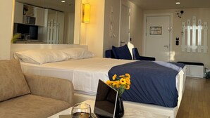 Une chambre d’hôtel avec deux lits, un canapé, une table avec un ordinateur portable, un verre à vin et un vase avec des fleurs.