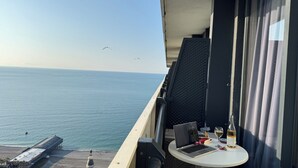 Un balcon avec vue sur la mer, une table avec un ordinateur portable, une bouteille de vin et un verre.