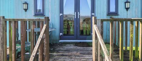 A wooden deck leading to a blue cabin with two windows and a door.