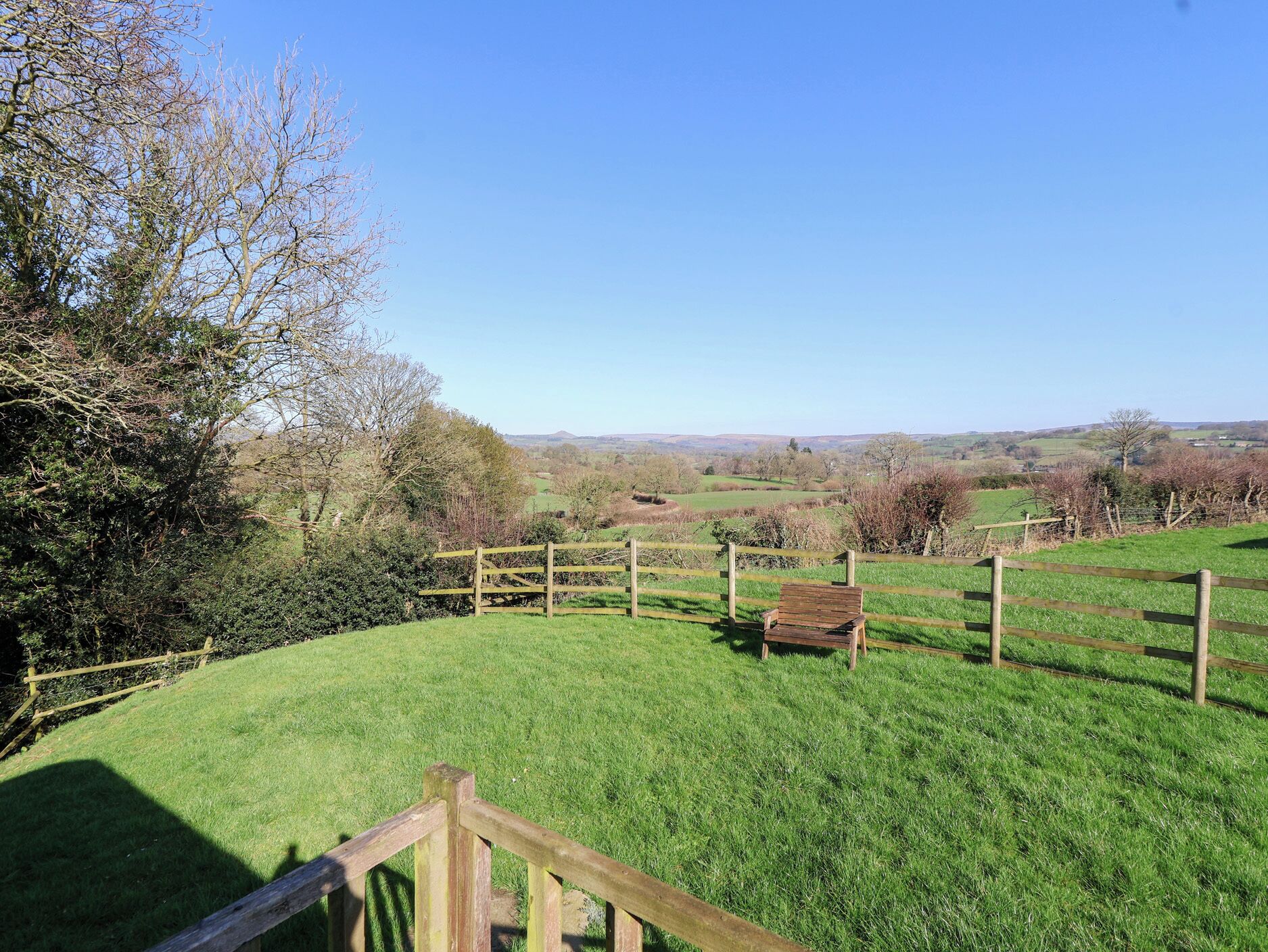 A rural landscape with a wooden fence, a bench, and a grassy field.