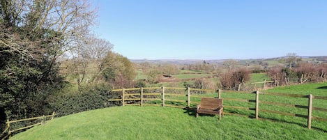 A rural landscape with a wooden fence, a bench, and a grassy field.