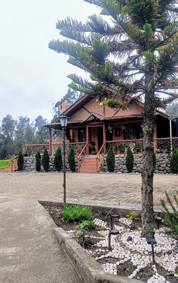 A rustic house with a stone foundation, a wooden porch, and a well-maintained garden with various plants and a pathway.