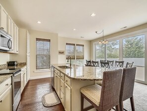 A kitchen with a central island, dining chairs, and a view of the outdoors. - Modern 4BR House near Bethany Beach | Decks & Pool (Bethany Beach)