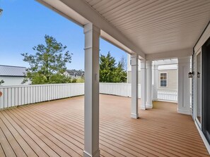 A covered wooden deck with white railings and columns, leading to a building entrance. - Modern 4BR House near Bethany Beach | Decks & Pool (Bethany Beach)