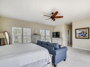 A bedroom with a bed, a blue sofa, a ceiling fan, a TV, and a painting on the wall. - Modern 4BR House near Bethany Beach | Decks & Pool (Bethany Beach)