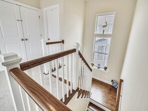 A staircase with wooden handrails and white walls, leading to a landing with a window and a bird decoration. - Modern 4BR House near Bethany Beach | Decks & Pool (Bethany Beach)