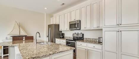 A kitchen with white cabinetry, granite countertops, a stainless steel refrigerator, a microwave, and a stove.