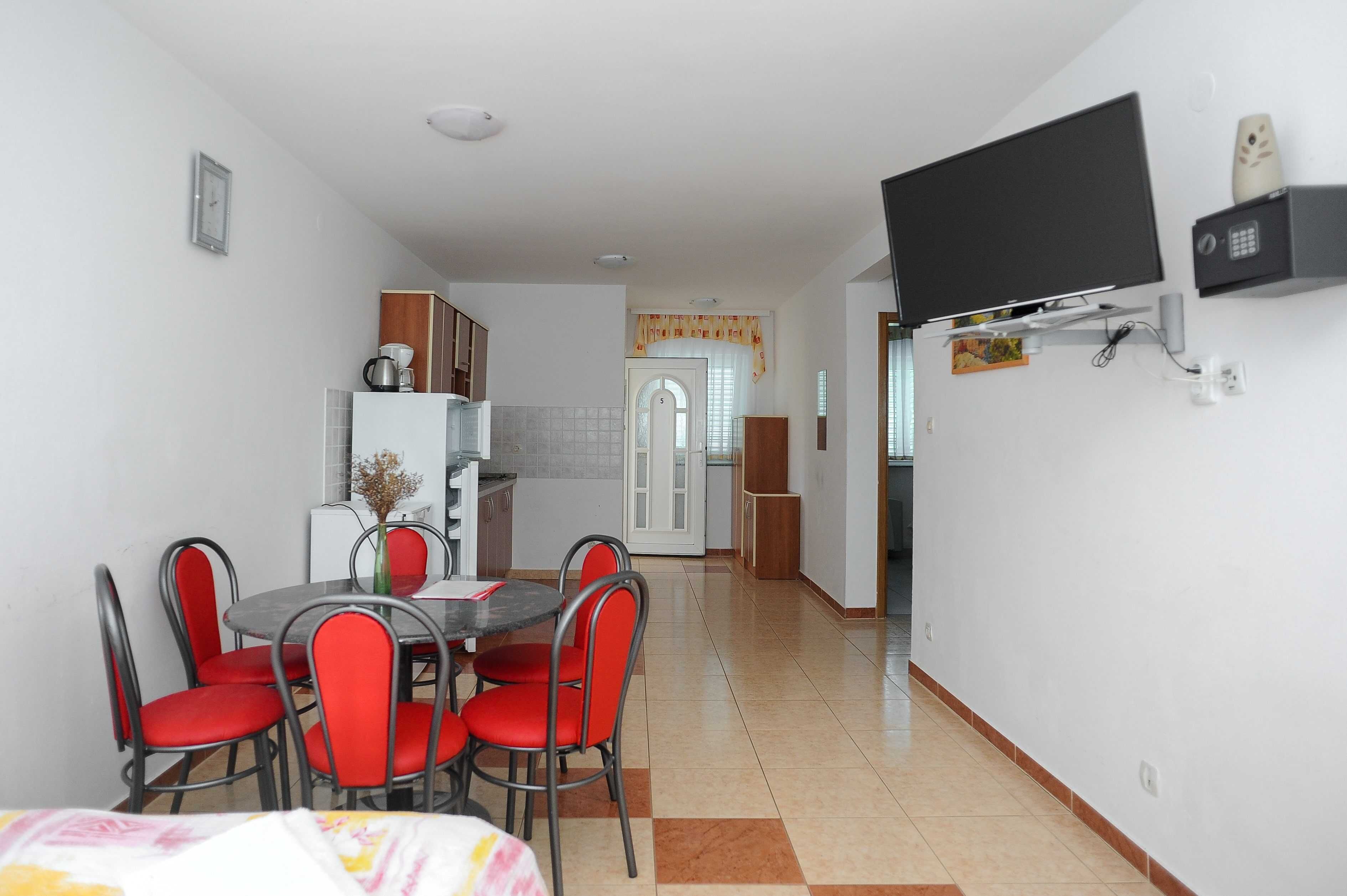A compact living space with a dining area, kitchenette, and a TV mounted on the wall.