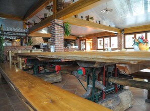 Un interior rústico con paredes de ladrillo visto, vigas de madera y una larga mesa de madera con estructura metálica inferior.